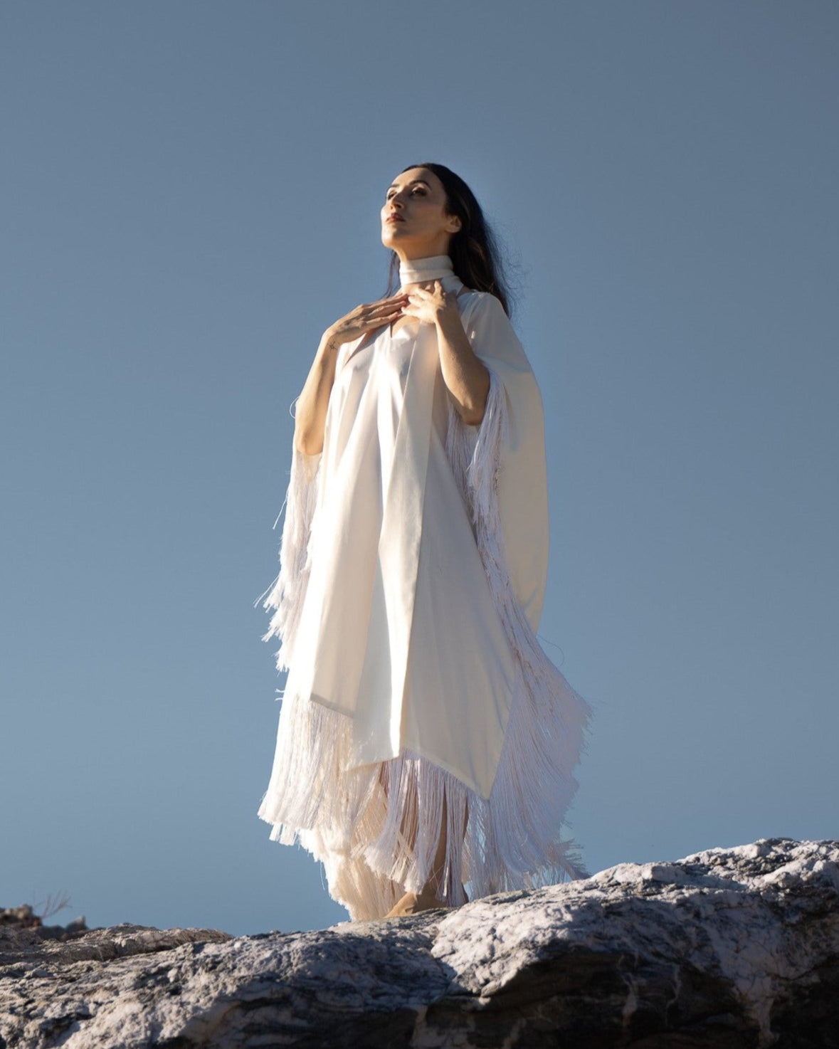 Woman in a white dress standing on rocks with a clear blue sky background